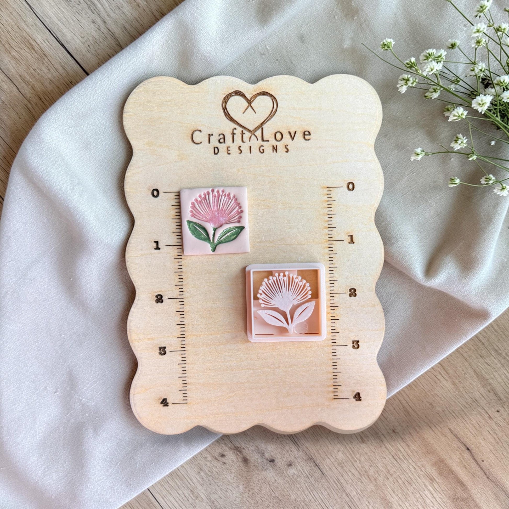 Cutter and finished clay piece displayed on a wooden measuring board with ruler markings and soft floral accents.