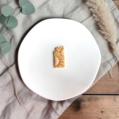Finished rectangular clay piece featuring sunflower design with gold-highlighted petals on a white plate.