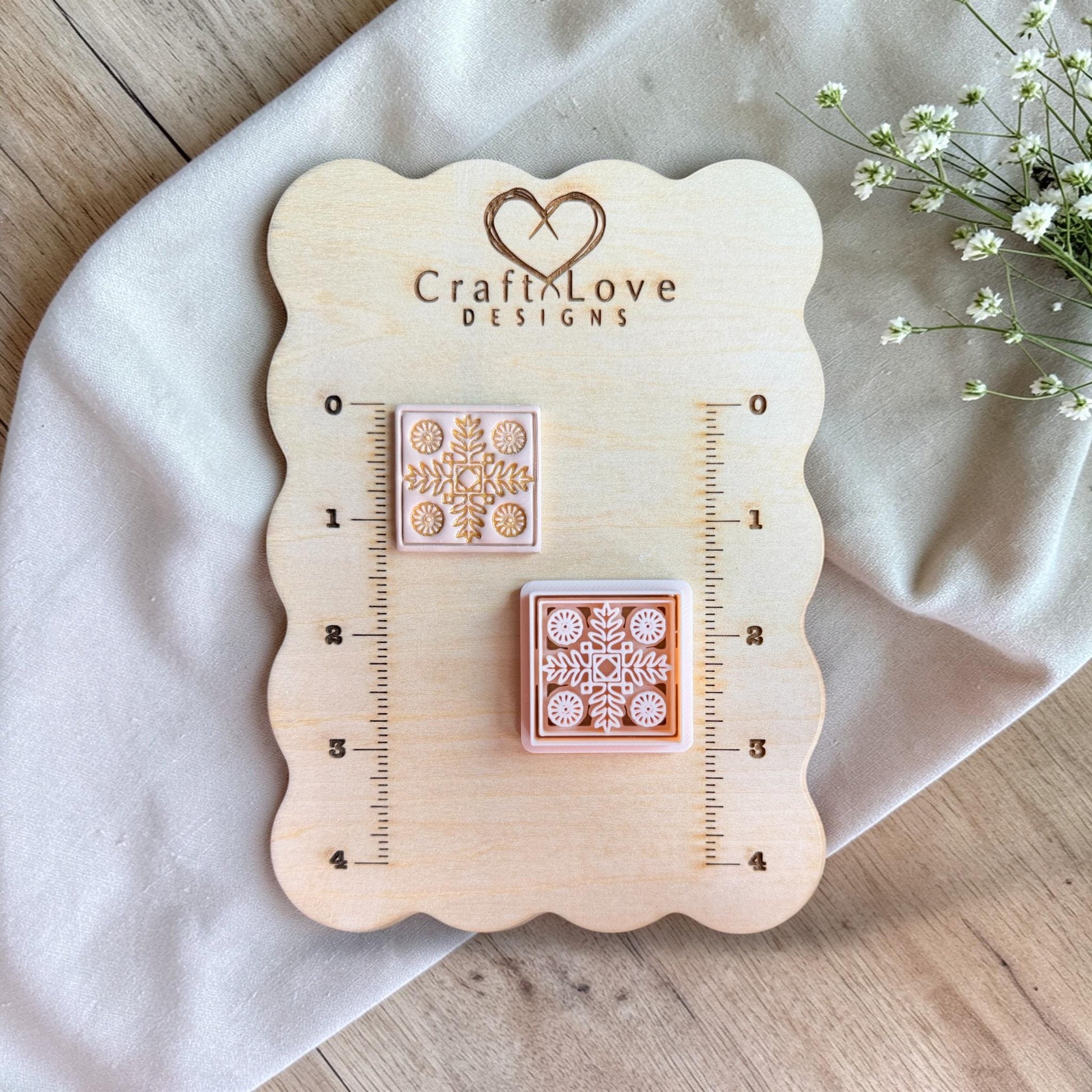 Cutter and finished clay piece displayed on a wooden measuring board with ruler markings and soft floral styling.