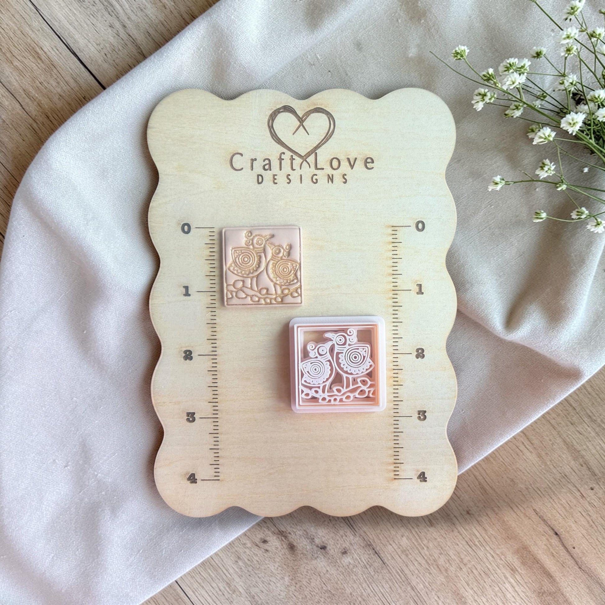 Cutter and finished clay piece displayed on a wooden measuring board with ruler markings and floral accents.