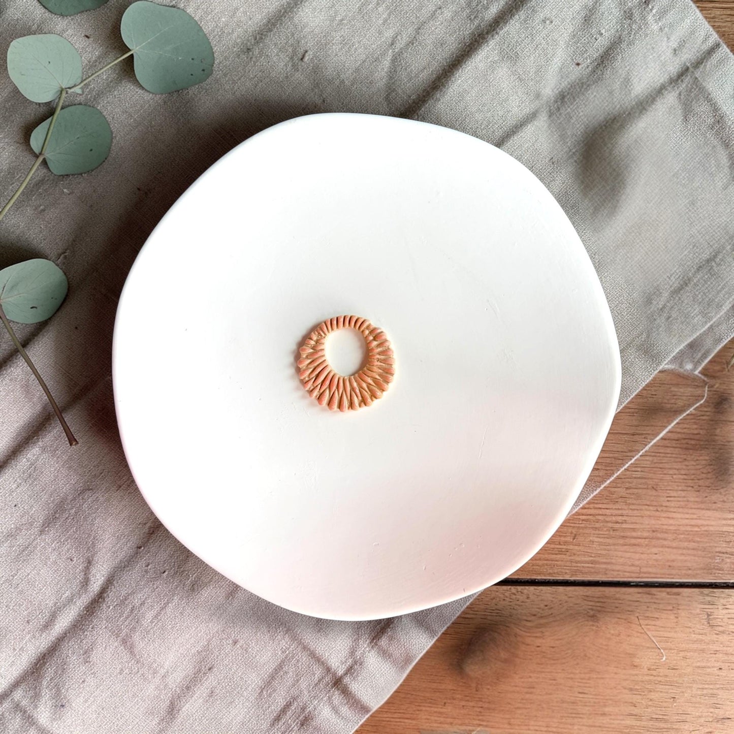 Finished circular clay piece with open center and textured radial pattern displayed on a white plate.