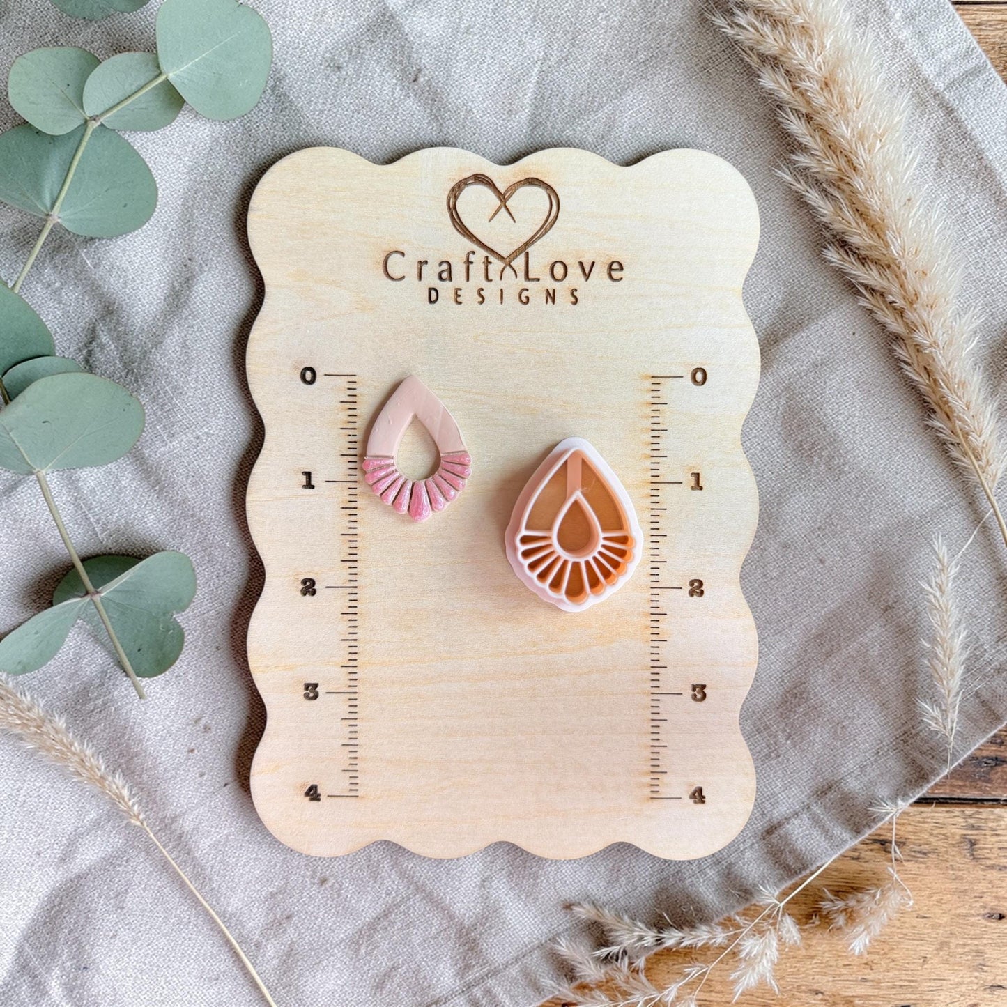 Cutter and finished clay piece displayed on a wooden measuring board with ruler markings and soft neutral styling.