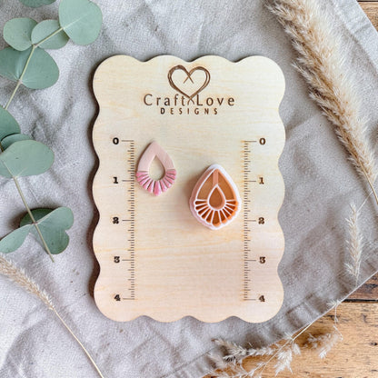 Cutter and finished clay piece displayed on a wooden measuring board with ruler markings and soft neutral styling.