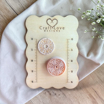 Cutter and finished clay piece displayed on a wooden measuring board with ruler markings and surrounding greenery.