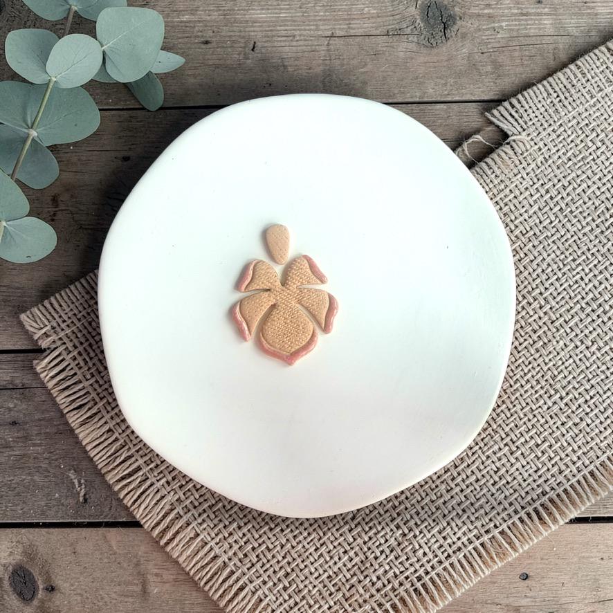 Finished clay earring with tropical flower design and textured center displayed on a white plate with woven fabric background.