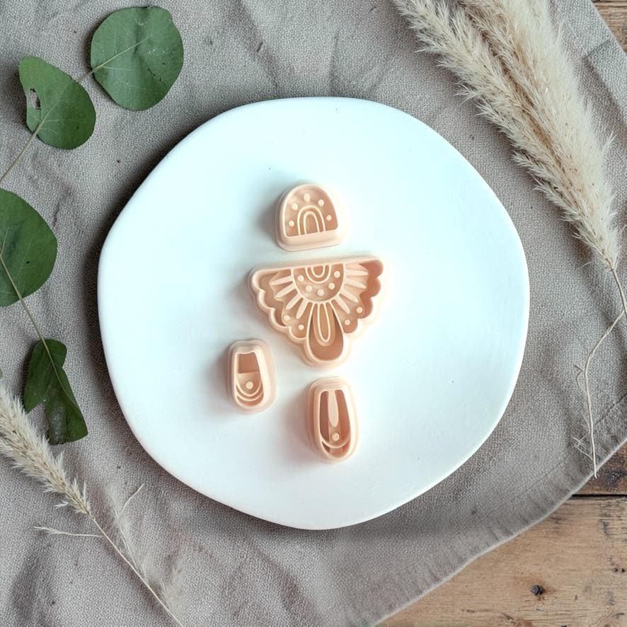 Polymer clay cutter set with boho sunburst arch shape, rainbow top piece, and two dangle connector shapes displayed on a white plate.
