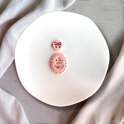 Close up of feminine anchor and bow polymer clay cutter design with scalloped oval frame on white background.