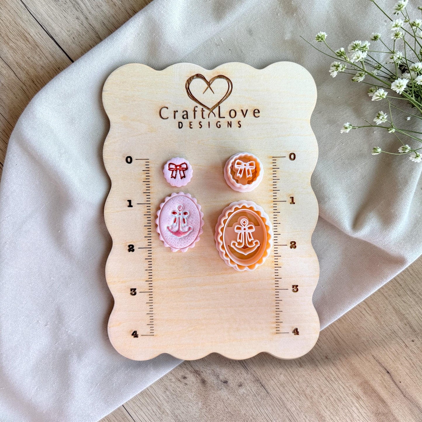 Anchor and bow polymer clay cutter set displayed on wooden measurement board with scalloped oval shapes and ruler size guide.