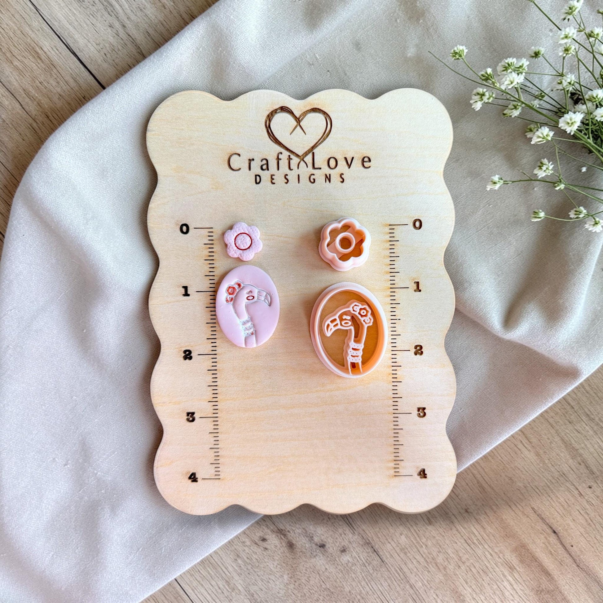 Flamingo and flower clay cutter set displayed on wooden measuring board with ruler for size reference.