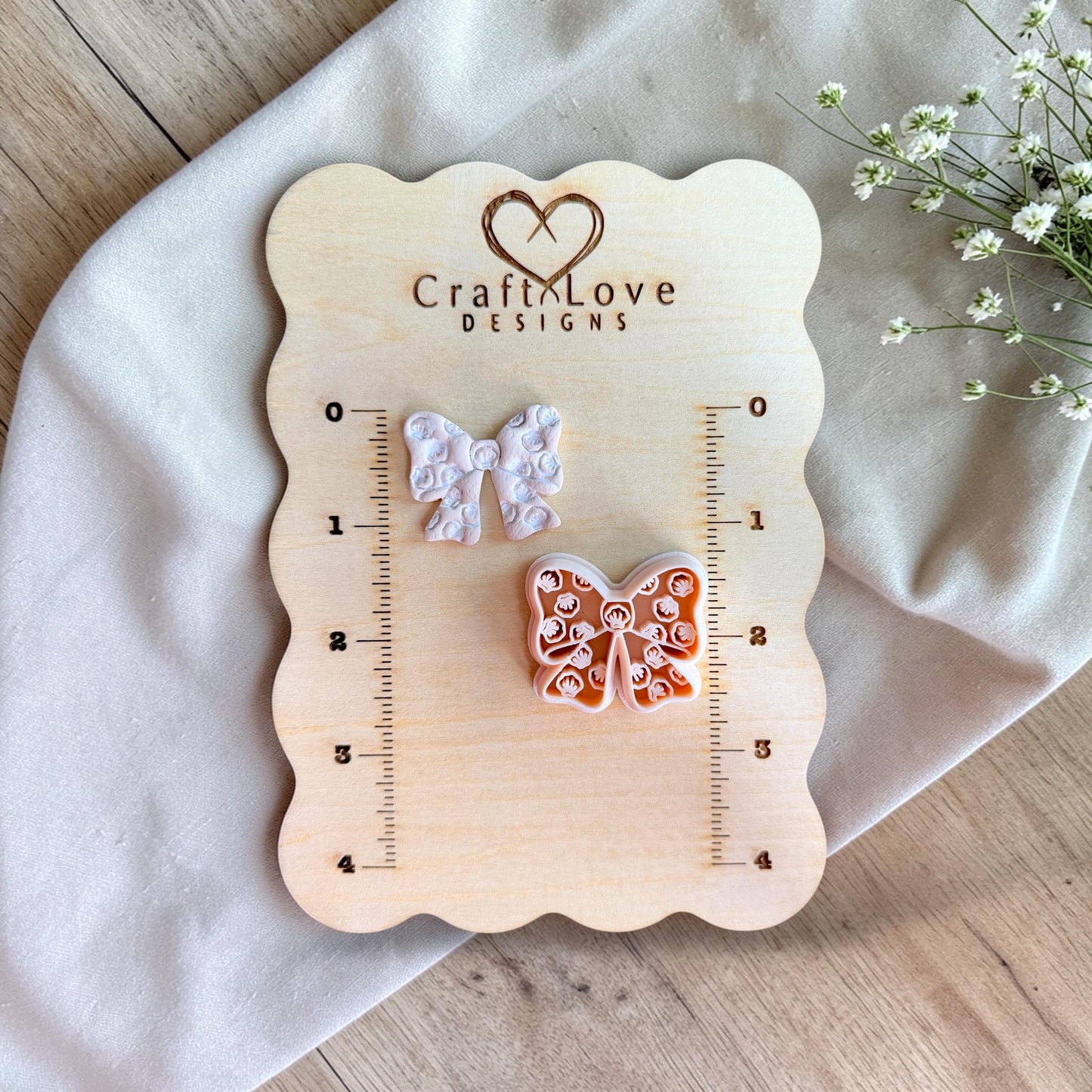 Seashell bow polymer clay cutter and finished clay bow displayed on wooden measurement board with ruler for size reference.