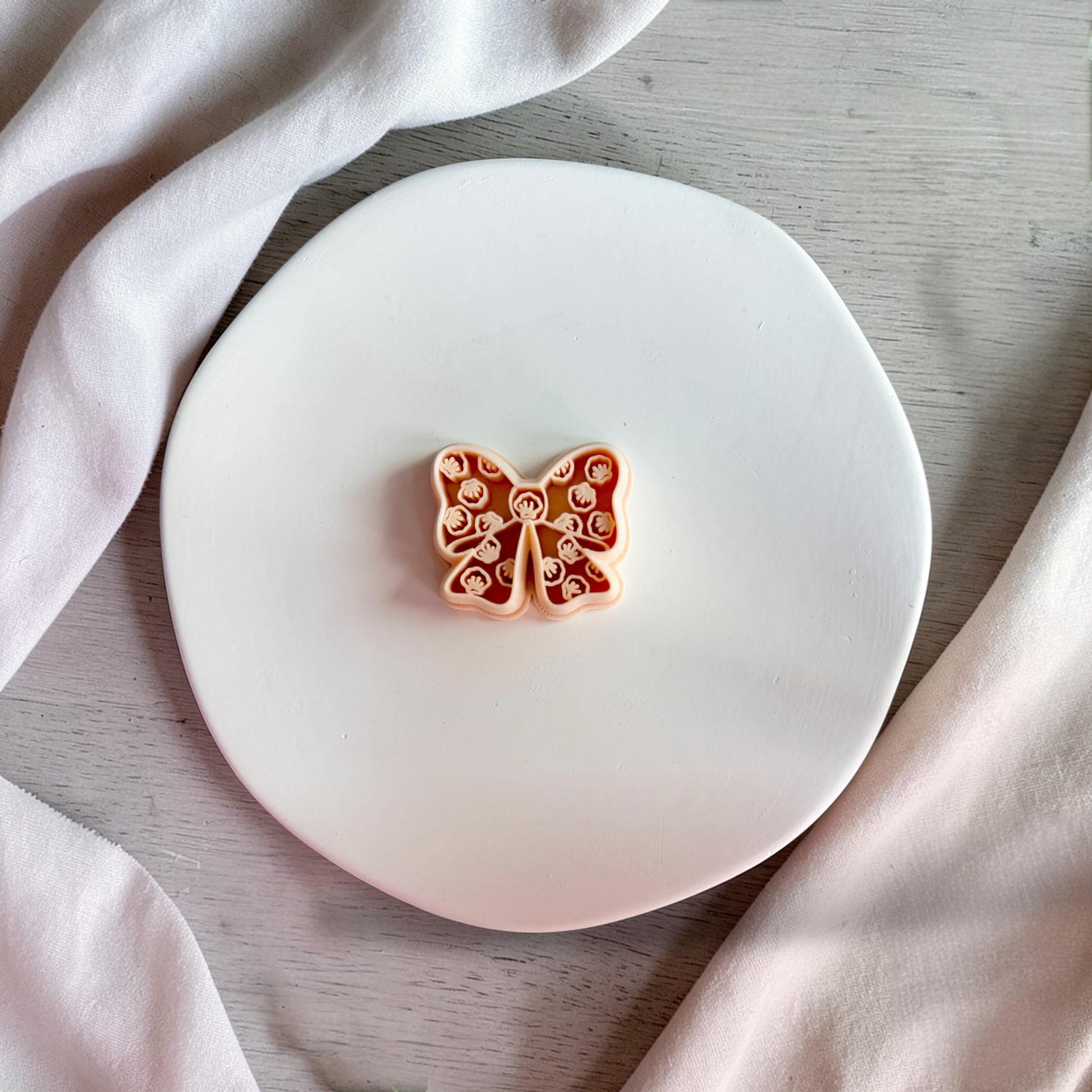 Detailed seashell bow polymer clay cutter on white plate showing intricate shell texture pattern.
