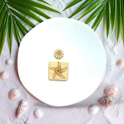 Starfish square polymer clay cutter with flower stud displayed on beach sand with shells and palm leaves