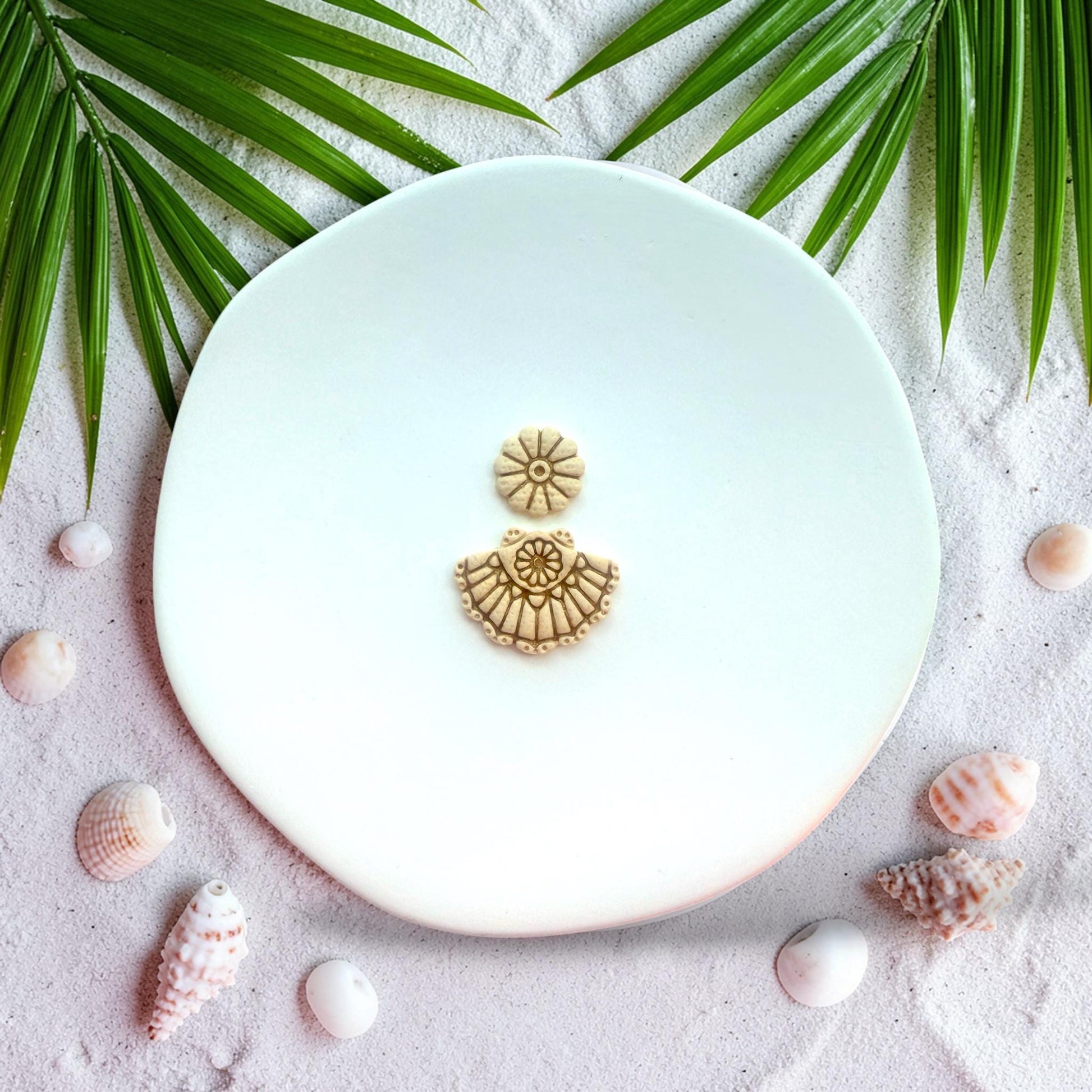 Finished clay earrings showing scallop fan shell design with floral stud top on white background