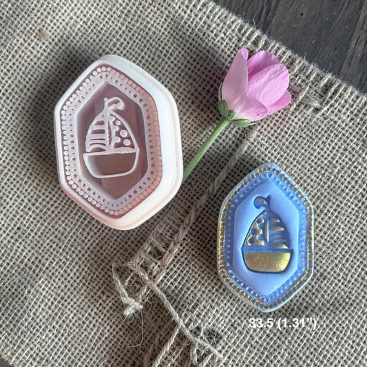 Sailboat polymer clay cutter with finished blue and gold example on textured fabric background