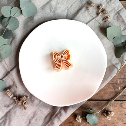 Bow polymer clay cutter on white plate with neutral fabric and greenery background
