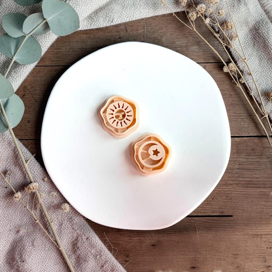 Sun and moon polymer clay cutters displayed on white plate with neutral fabric and greenery