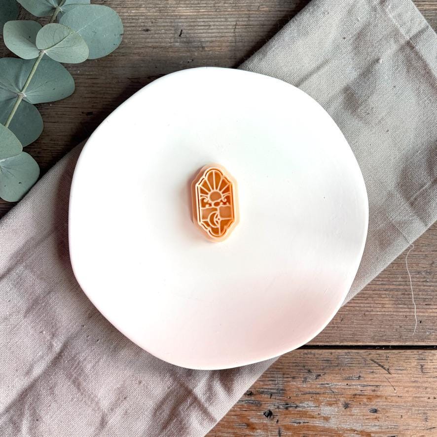 Sky and moon clay piece on white plate with neutral fabric background