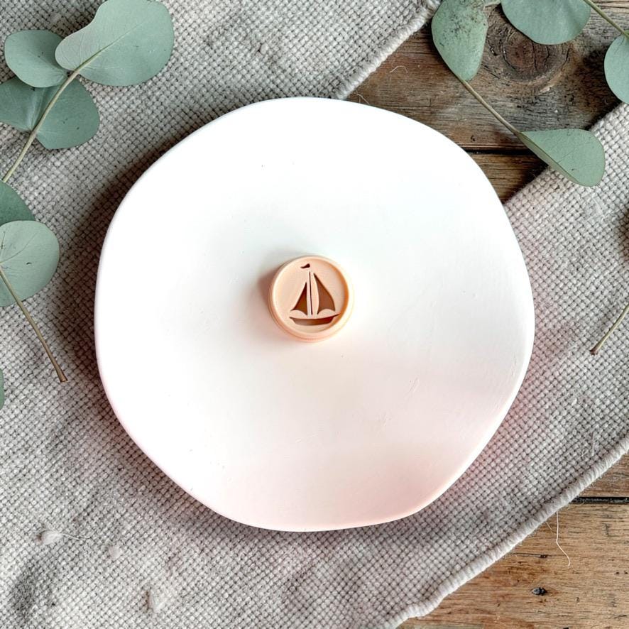 Sailboat polymer clay cutter on white plate with neutral fabric and greenery