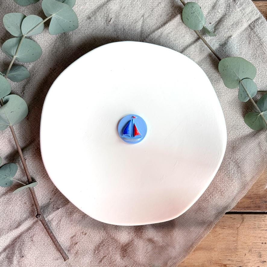 Blue sailboat clay piece on white plate showing embossed detail