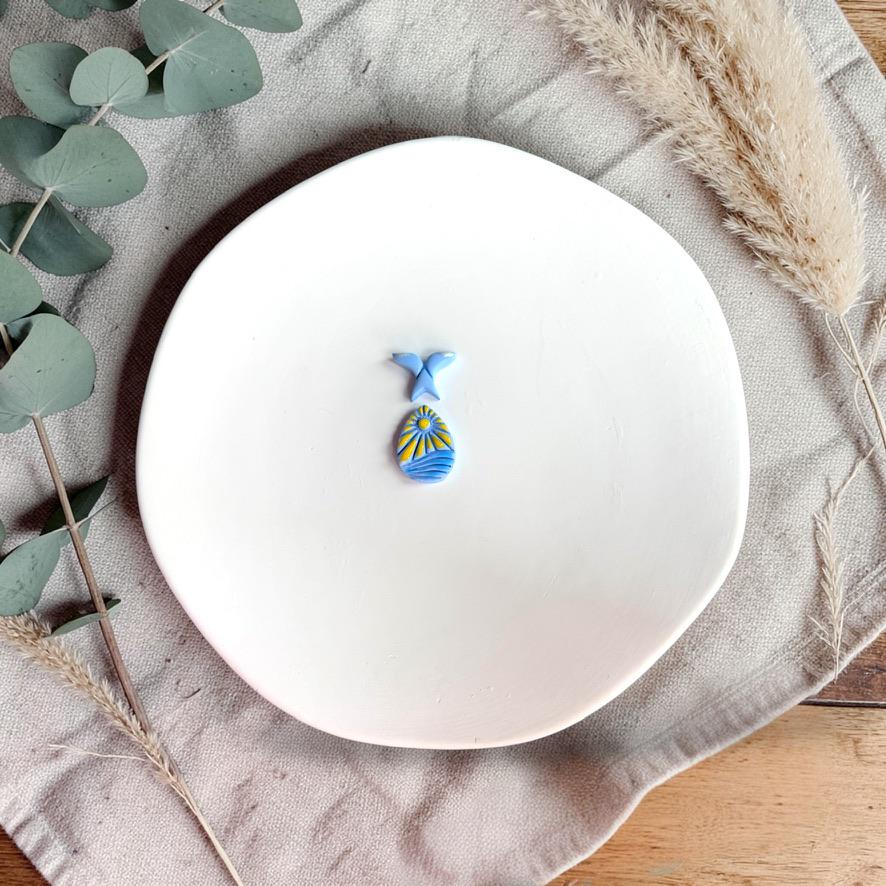 Blue clay earrings with whale tail top and ocean scene bottom on white plate