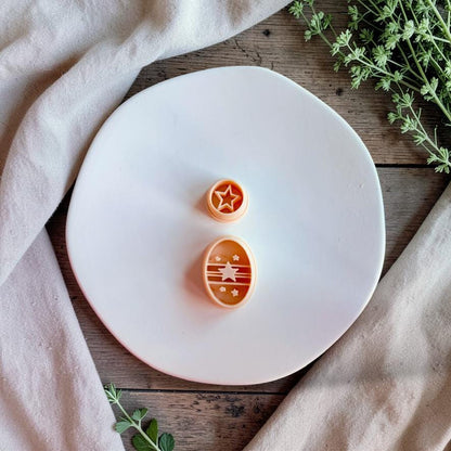 Star and striped oval polymer clay cutters on white plate with neutral fabric and greenery