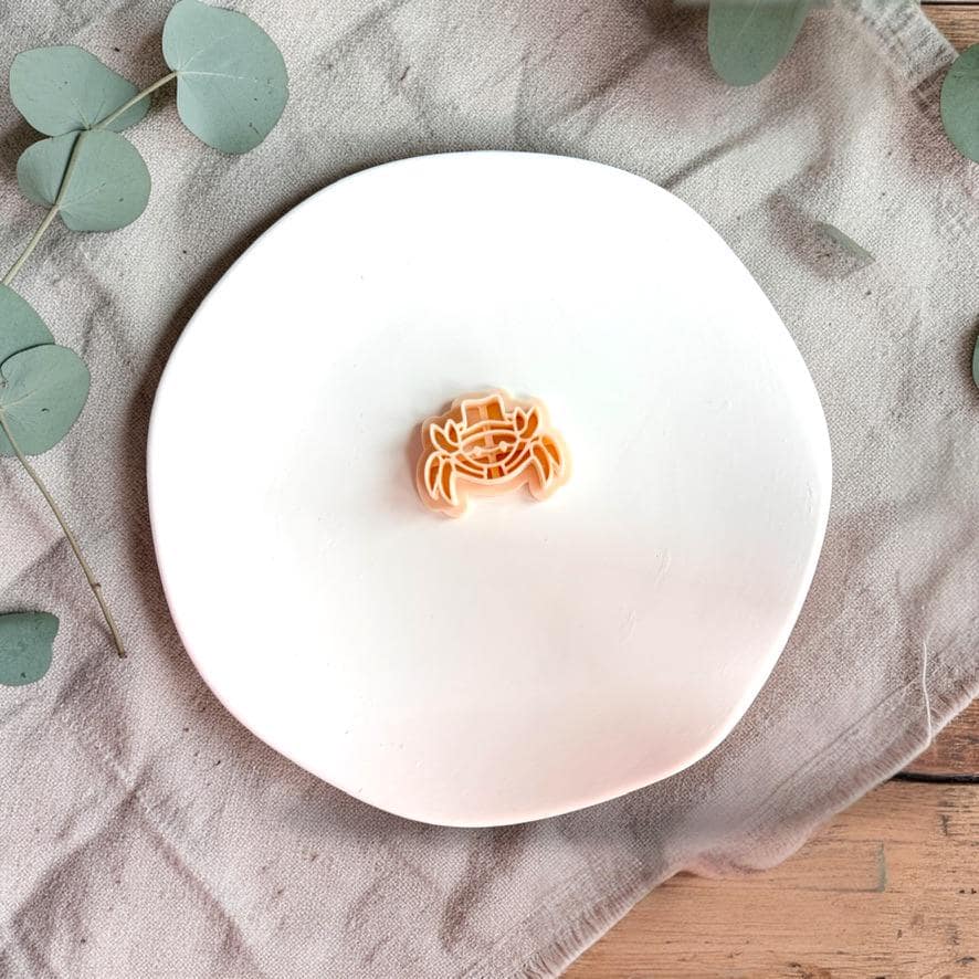 Crab polymer clay cutter with hat displayed on white plate with neutral fabric background