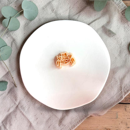 Crab polymer clay cutter with hat displayed on white plate with neutral fabric background