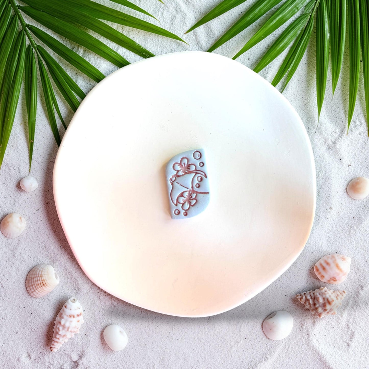 Stingray polymer clay cutter with floral details on beach styled background with shells and palm leaves