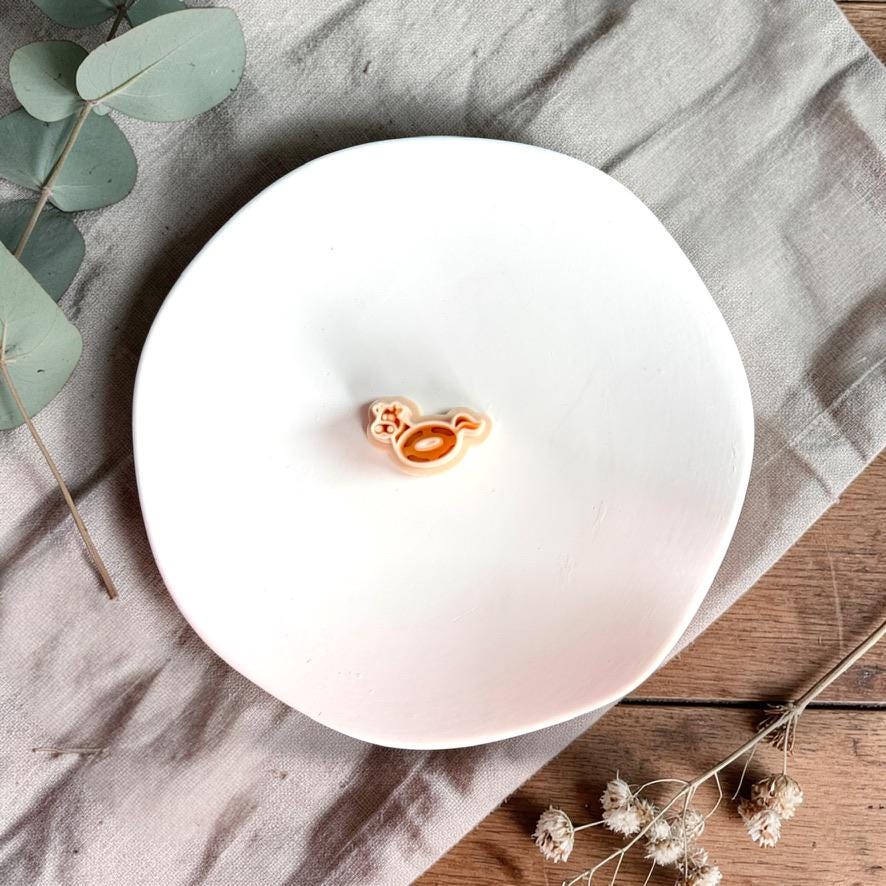 Cow shaped pool float polymer clay cutter on white plate with neutral fabric and greenery