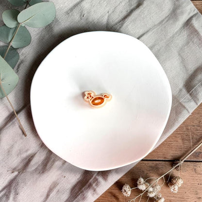 Cow shaped pool float polymer clay cutter on white plate with neutral fabric and greenery