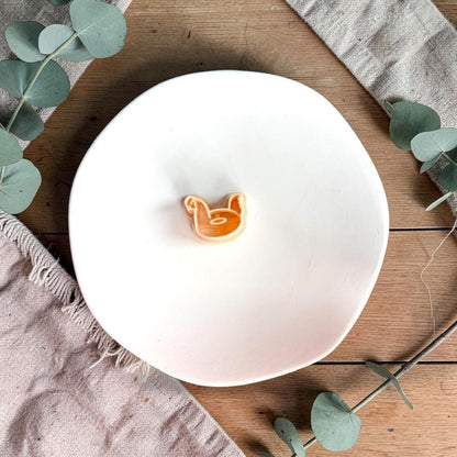 Chicken floatie polymer clay cutter displayed on white plate with neutral fabric and greenery