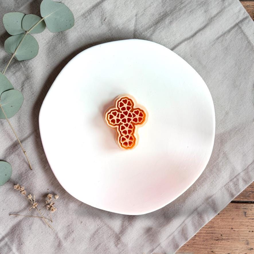 Floral cross polymer clay cutter shown on white display plate with neutral linen background