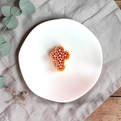 Floral cross polymer clay cutter shown on white display plate with neutral linen background