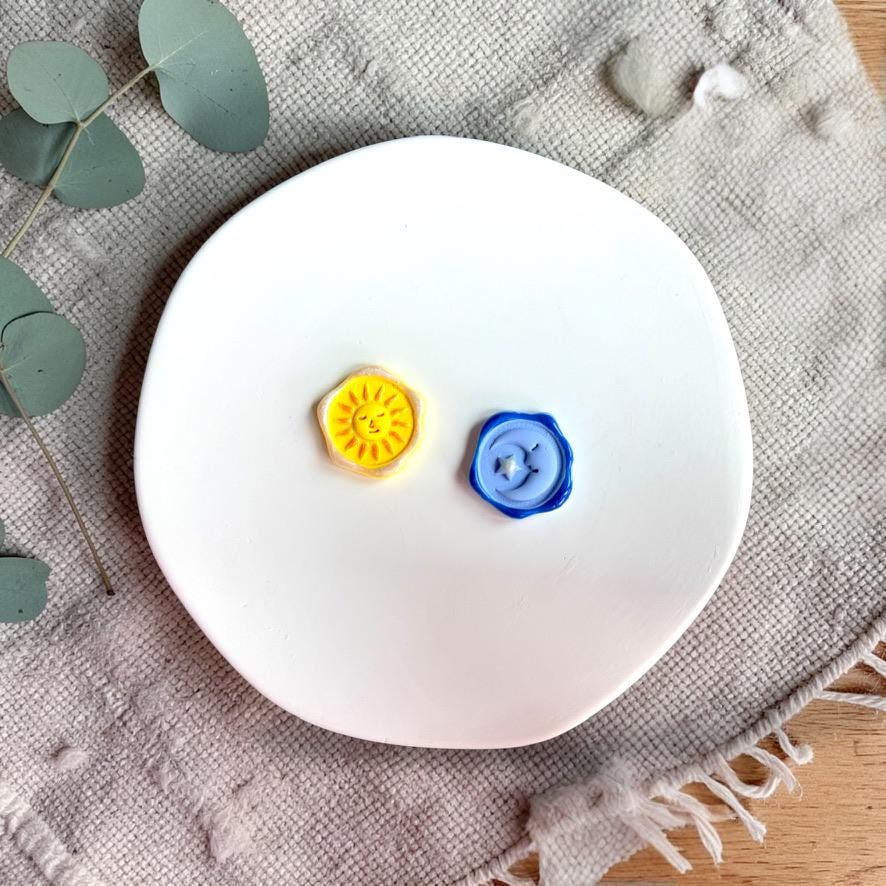 Finished sun and moon clay pieces in yellow and blue on white plate with textured fabric
