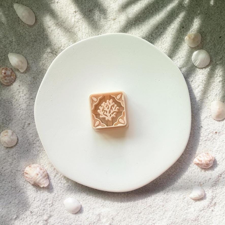 Coral tile polymer clay cutter shown on white plate with beach sand and shells background