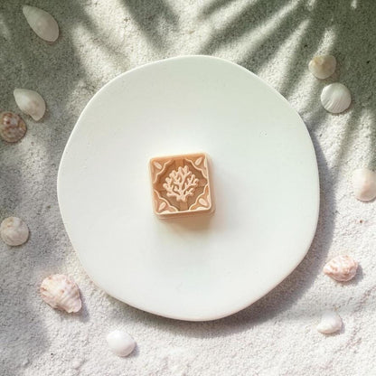 Coral tile polymer clay cutter shown on white plate with beach sand and shells background