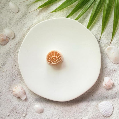 Spiral seashell polymer clay cutter displayed on white plate with beach themed background