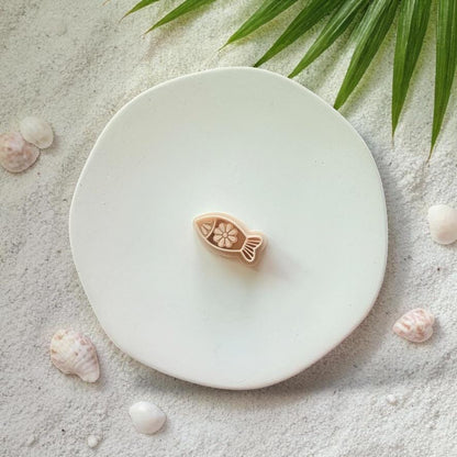Fish clay cutter on white plate with sand, seashells, and tropical leaves