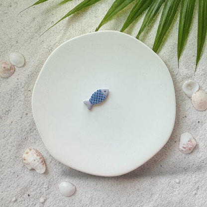Blue fish clay piece with textured scales on white plate beach background
