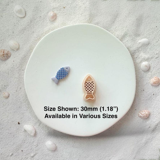 Fish cutter and finished clay pieces with size text 30mm on white plate with sand and shells