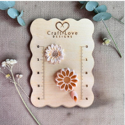 Sunflower clay sample with petal detail next to cutter and petal tool on wooden measurement board