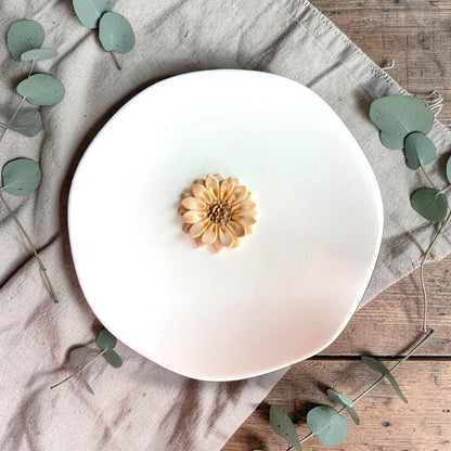 Finished sunflower clay piece centered on white plate with neutral fabric background