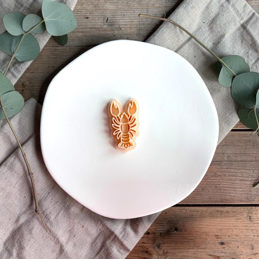 Lobster polymer clay cutter on white plate with neutral fabric and greenery