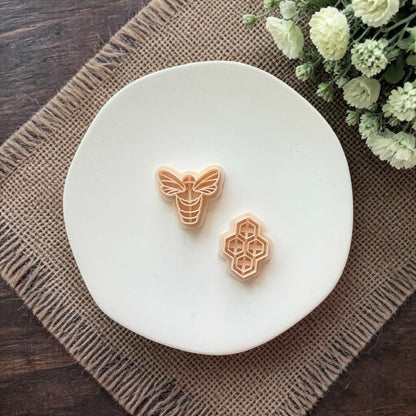 small bee shaped clay earring on white plate with rustic fabric background