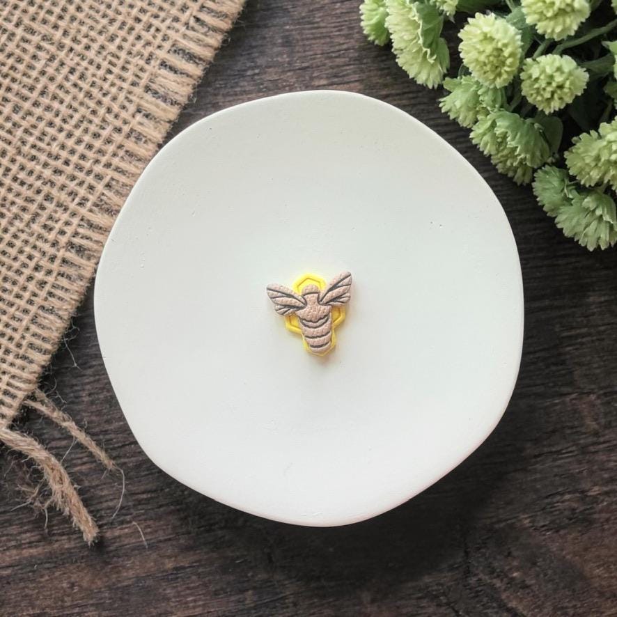 small bee shaped clay earring on white plate with rustic fabric background