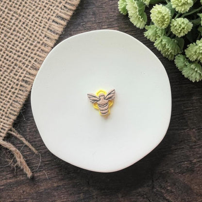 small bee shaped clay earring on white plate with rustic fabric background