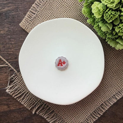 small A plus clay earring on white plate with burlap background