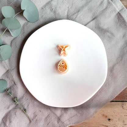 Whale tail and ocean scene polymer clay cutters on white plate with neutral fabric and greenery