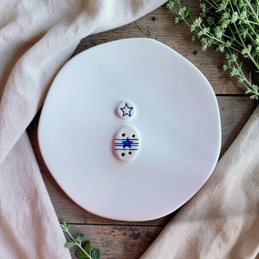 Finished patriotic clay earrings with star top and striped oval bottom on white plate