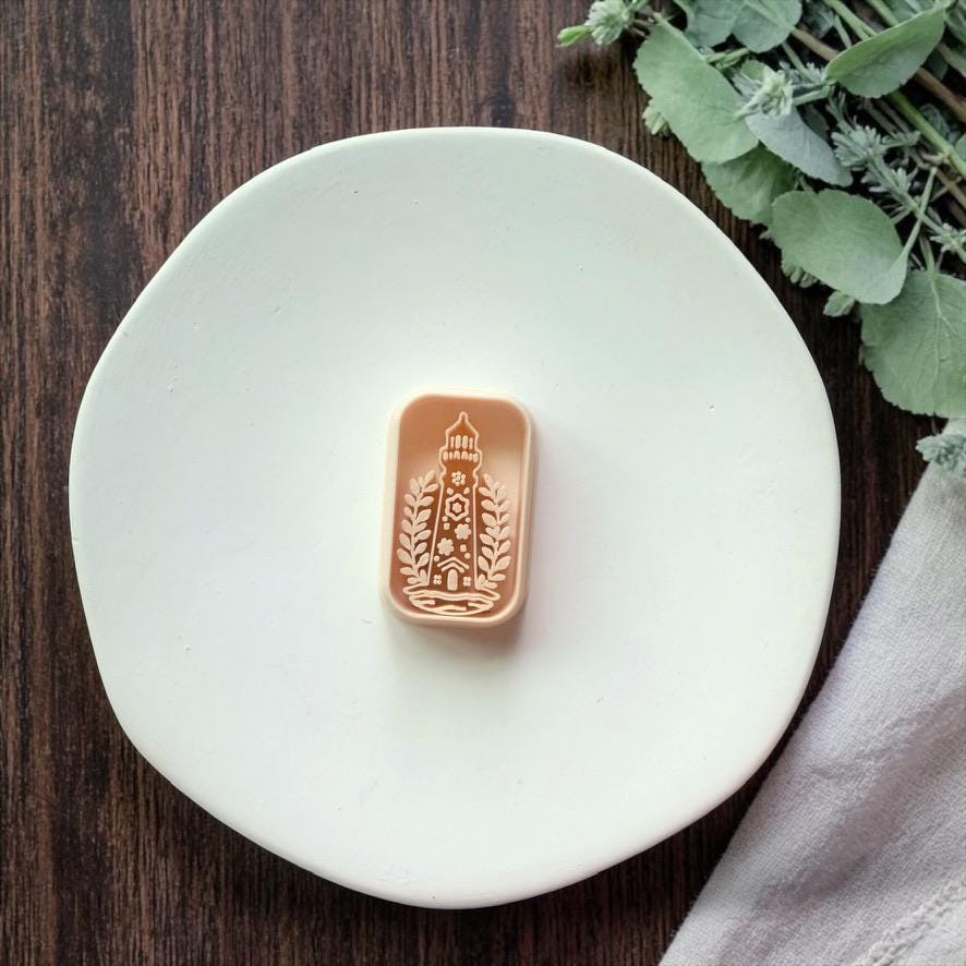 lighthouse polymer clay cutter on white plate with greenery and wood background